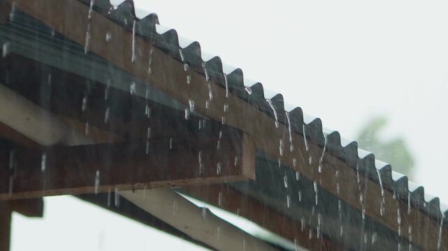 Heavy monsoon rain pouring over old zinc roof, water droplets splashing and flowing down weathered corrugated metal surface
