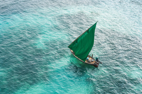 Aerial view of a traditional wooden dhoni boat with a vibrant green sail navigating the clear turquoise waters of the Indian Ocean, Vaikaradhoo, Haa Dhaalu City, Maldives.