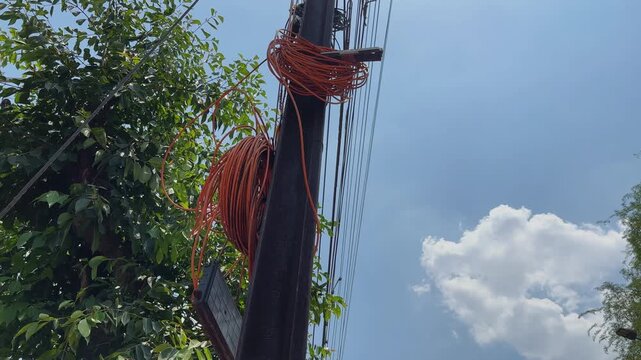 Coiled fiber optic cables mounted on a utility pole with overhead communication lines showcasing telecom infrastructure network maintenance and urban connectivity beneath a clear sky