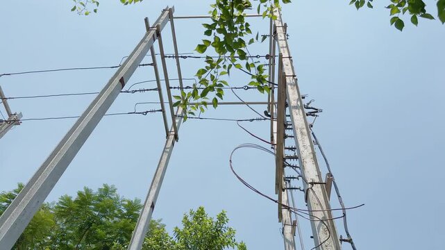 Low angle tracking shot of utility power poles and overhead electrical lines against a clear blue sky with surrounding trees highlighting urban energy distribution infrastructure networkeds