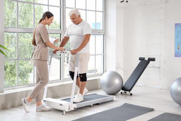 Fototapeta premium Senior man training with therapist on treadmill in rehabilitation center