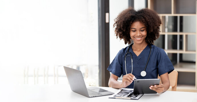 Smiling young African American female doctor using digital tablet at desk