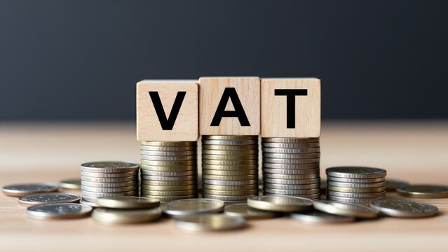VAT Concept: Wooden blocks spelling out VAT stand atop stacks of coins, representing the financial concept of value-added tax and its economic impact.