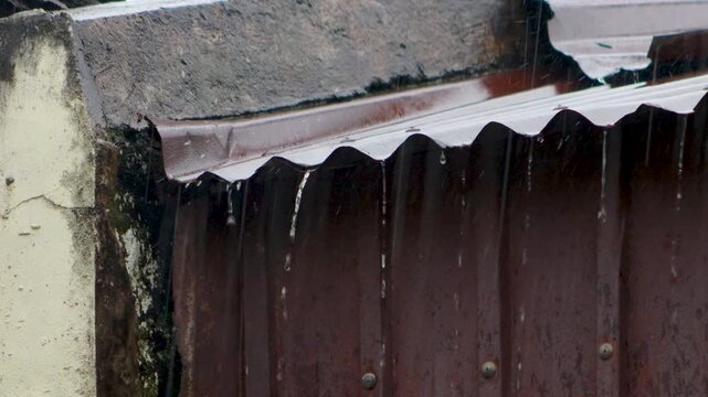 Heavy rain water droplets flowing through zinc metal roof, dramatic rainfall streaming down corrugated iron rooftop