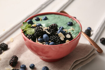 Obraz premium Napkin, bowl with tasty spirulina smoothie and berries on white background, closeup