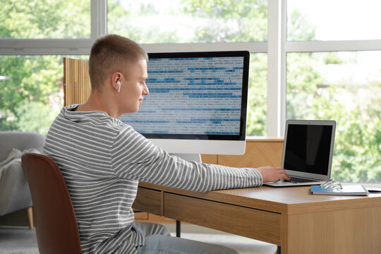 Young male programmer working with computer and laptop in modern home office
