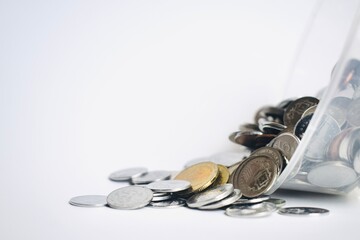 Low angle shot of various Malaysian sen coins tumbling and pouring out from a transparent container against a bright white background. © Akram