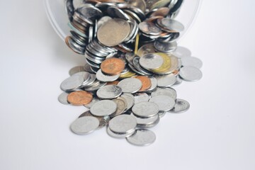 High angle view of a collection of mixed Malaysian coins spilling out from a clear plastic jar onto a white background, symbolizing savings, finance, and investment. © Akram