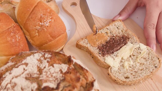 Spreading Peanut Butter on Multigrain Bread with Assorted Bakery Loaves