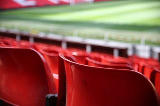 Empty Red Stadium Seats in a Vibrant Sports Arena with Bright Natural Light and a Blurred Green Field Background for Event Promotion.