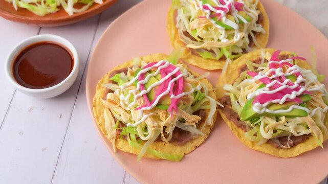 Aerial view of Mexican food, chicken tostadas with avocado, pickled red onion and cream on a pink plate