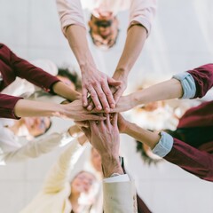 Obraz premium Group of people stacking hands in a tight circle for a teamwork and unity concept, viewed from overhead with a luminous and warm amber glow
