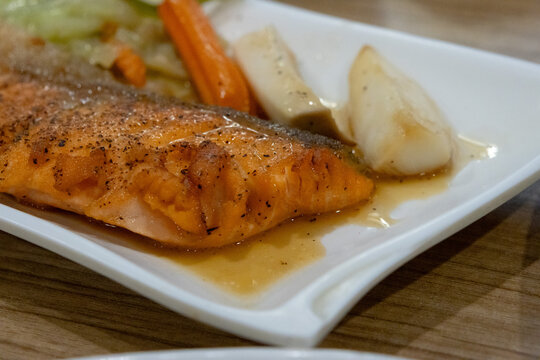 A perfectly cooked salmon fillet on a white plate with mixed vegetables