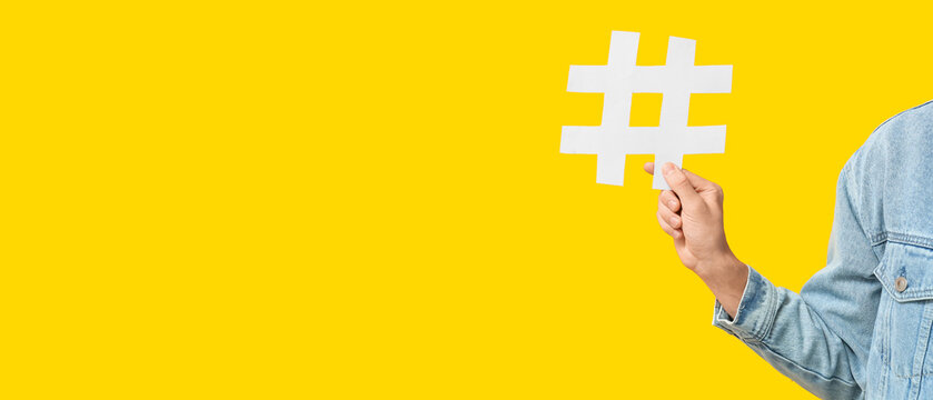Hand of young man with hashtag symbol on yellow background