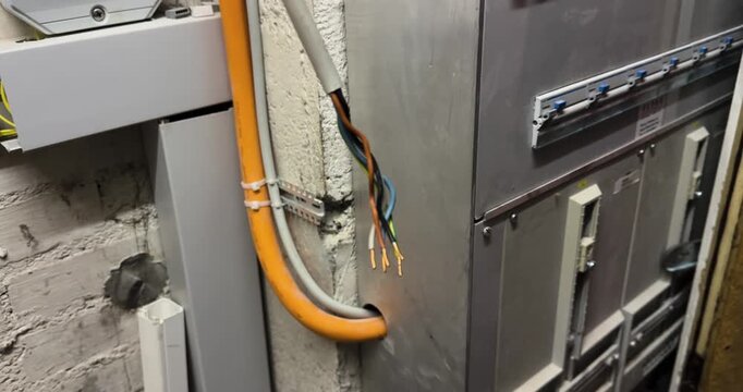 exposed electrical wires protruding from a wall near an electrical installation in a utility room. Concept of electrical hazard, electric shock risk, workplace safety, faulty wiring, maintenance