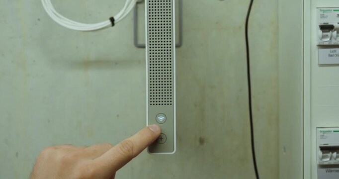 Close-up of a hand pressing the WLAN activation button on a network router installed in a technical control room. Concept of wireless internet, network connectivity, broadband access