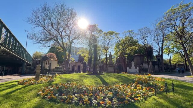 Beautiful view of the Montmartre cemetery with its ancient tombs, lush trees, and colorful flower beds under a bright blue sky, a famous landmark and popular tourist destination in Paris