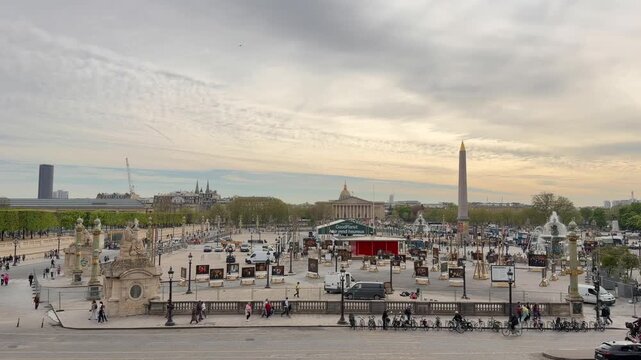 Wide view of the iconic Place de la Concorde in Paris with the Luxor Obelisk, tourists walking, and cars driving around the square under a cloudy sky during a beautiful spring day