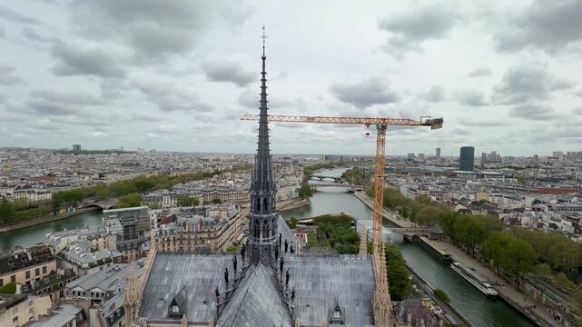 Aerial view tracking down the famous spire of Notre Dame Cathedral, revealing the intricate gothic architecture and the surrounding Paris cityscape with the River Seine flowing below