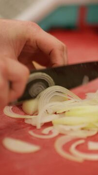 Vertical video. Chopping onion. Slicing vegetable. Chef hand professionally cutting raw fresh white spicy ingredient with knife on red board restaurant kitchen.