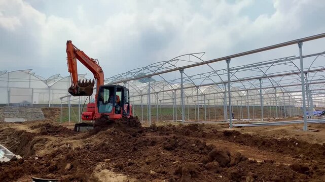 Close-up footage of an excavator crawler track moving across soil during greenhouse construction and land development work