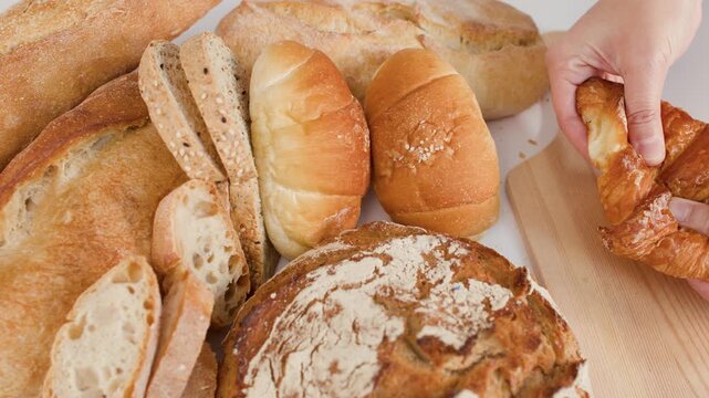 Hands Breaking Fresh Flaky Croissant Over Assorted Bakery Breads
