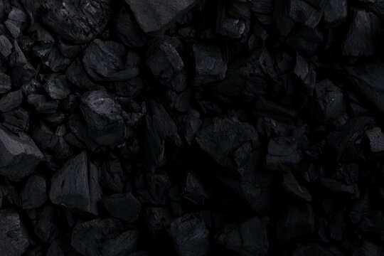 Close-up of irregular black charcoal pieces with rough textures and matte surfaces, arranged densely together.