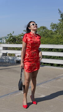 Asian woman poses outdoors wears a modern red mini cheongsam with gold floral embroidery
