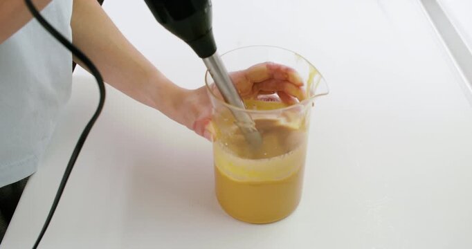 Kitchen appliance. Blending sauce. Chef hand mixing yellow liquid in glass beaker with professional electric device on white table.