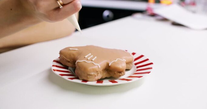 Garnishing pastry. Piping icing. Female confectioner hand drawing white lines sugar frosting decorating glazed gingerbread cookie.