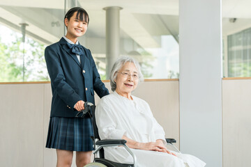 A junior high school girl in uniform and her grandmother in a wheelchair visit a nursing home or hospital.