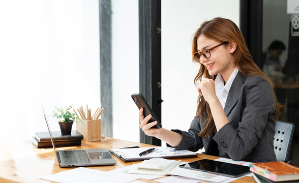 Cheerful young businesswoman looking at smartphone at her office desk