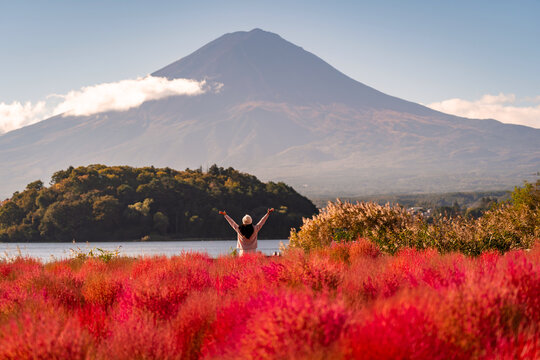 Joyful tourist woman in a vibrant red kochia field enjoying the scenic landscape of Mount Fuji and Lake Kawaguchiko, Japan
