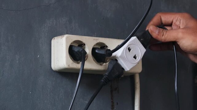 Person disconnecting multiple electrical plugs from a wall outlet. Energy saving and home electricity management concept with focus on reducing power consumption and improving electrical safety.