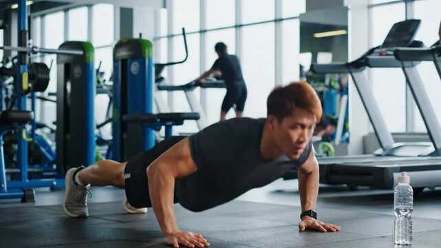 Focused Asian man doing push-ups on gym floor, full body workout with fitness and training.