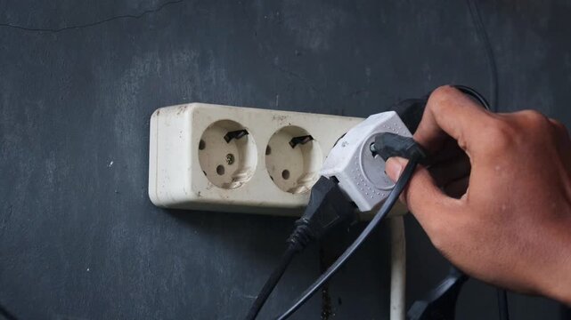 Person disconnecting multiple electrical plugs from a wall outlet. Energy saving and home electricity management concept with focus on reducing power consumption and improving electrical safety.