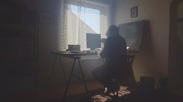 Sunlight streams into a dark room while a middle-aged man sits appearing agitated and troubled. Suitable for themes of stress, anxiety, frustration, and emotional conflict.