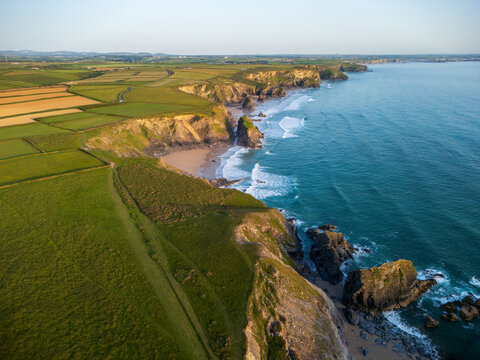 Aerial view of Pentire Steps Beach featuring rugged cliffs, green coastal fields, and sea stacks along the turquoise Atlantic coastline in Newquay, England, United Kingdom.