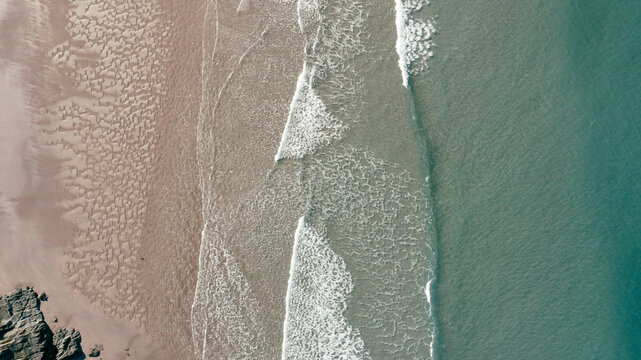 Aerial view of waves crashing on the sandy shore with turquoise water and coastal rocks near Burgh Island in Kingsbridge, Devon, United Kingdom.