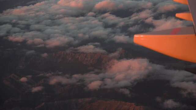 An aerial look through a plane window showing pink sunset clouds over mountain peaks.