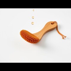 Fototapeta premium Wooden handle brush with orange bristles. Water droplets fall above it. Cleanliness concept, spa treatment, body care product.
