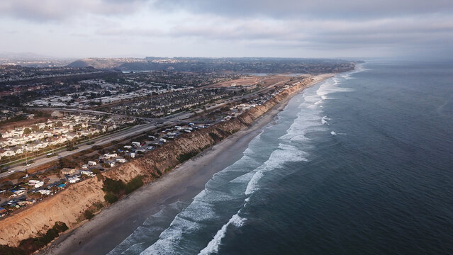 Aerial view of the coastline featuring a highway running parallel to the beach, an RV park situated on the cliffs, and waves breaking on the shore in Carlsbad, California, United States.