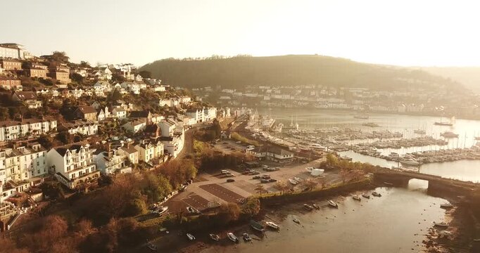 Aerial view of the coastal town of Kingswear with its historic buildings, marina filled with boats, and calm harbor waters during golden hour in Kingswear, England, United Kingdom.