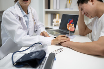 Fototapeta premium Doctor listens attentively to patient's concerns. Patient appears stressed, holding head in discomfort. Laptop displays detailed heart anatomy for discussion. Medical setting features stethoscope