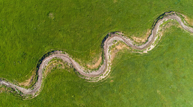 Vibrant green pasture fields neatly divided by empty naturally meandering dry creek bed channel backdrop