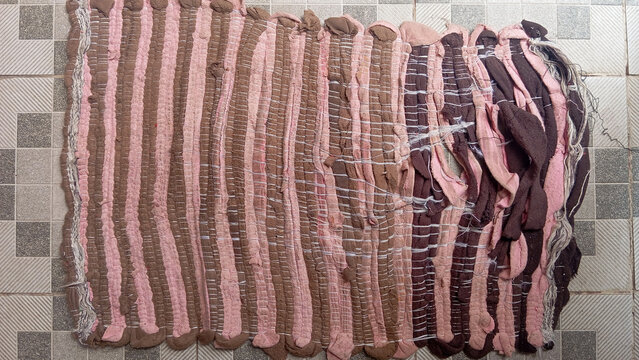 Worn woven fabric doormat in brown and pink colors placed on a patterned ceramic tile floor.