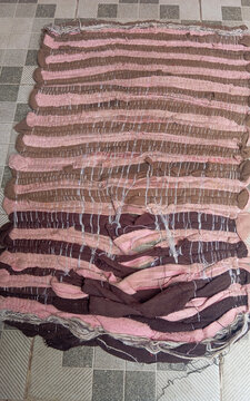 Worn woven fabric doormat in brown and pink colors placed on a patterned ceramic tile floor.