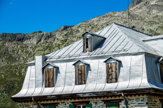 Aerial view of the historic building at Furka Pass with its distinctive metal roof and wooden shutters set against the rugged mountain slopes of Obergoms, Valais, Switzerland.