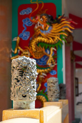 Ornate stone pillar in front of a vibrant dragon mural at a temple © Thanakrit