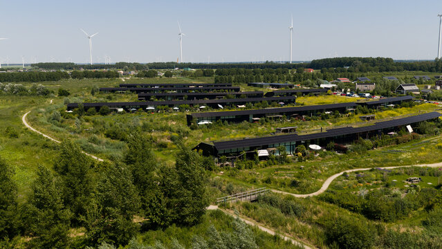 Aerial view of 't Eemgoed in Oosterwold, featuring sustainable modern housing integrated into a lush green landscape with wind turbines in the background in Almere, Flevoland, Netherlands.